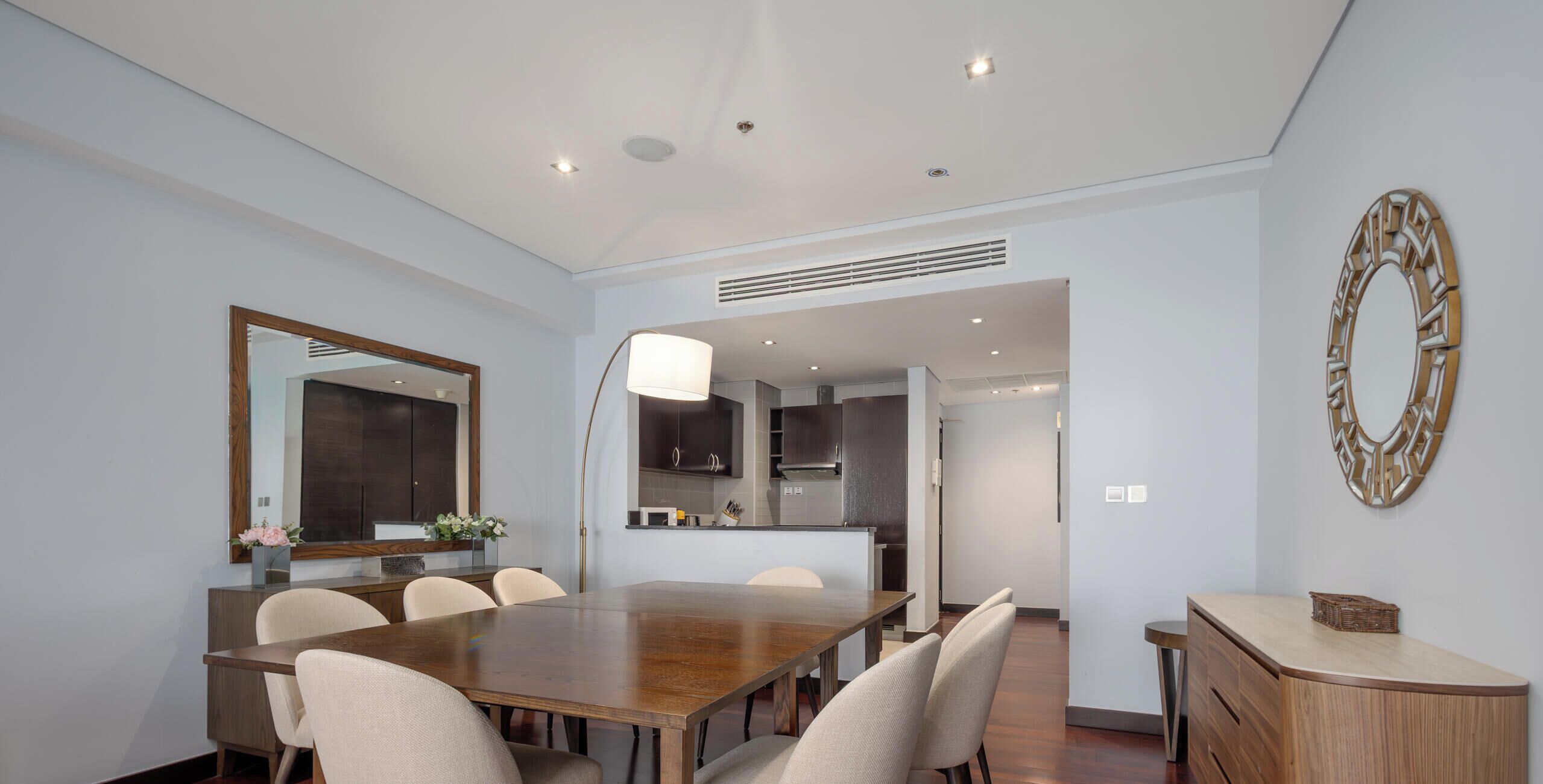 A modern dining room with a wooden table, six chairs, a large mirror, and a decorative wall piece.