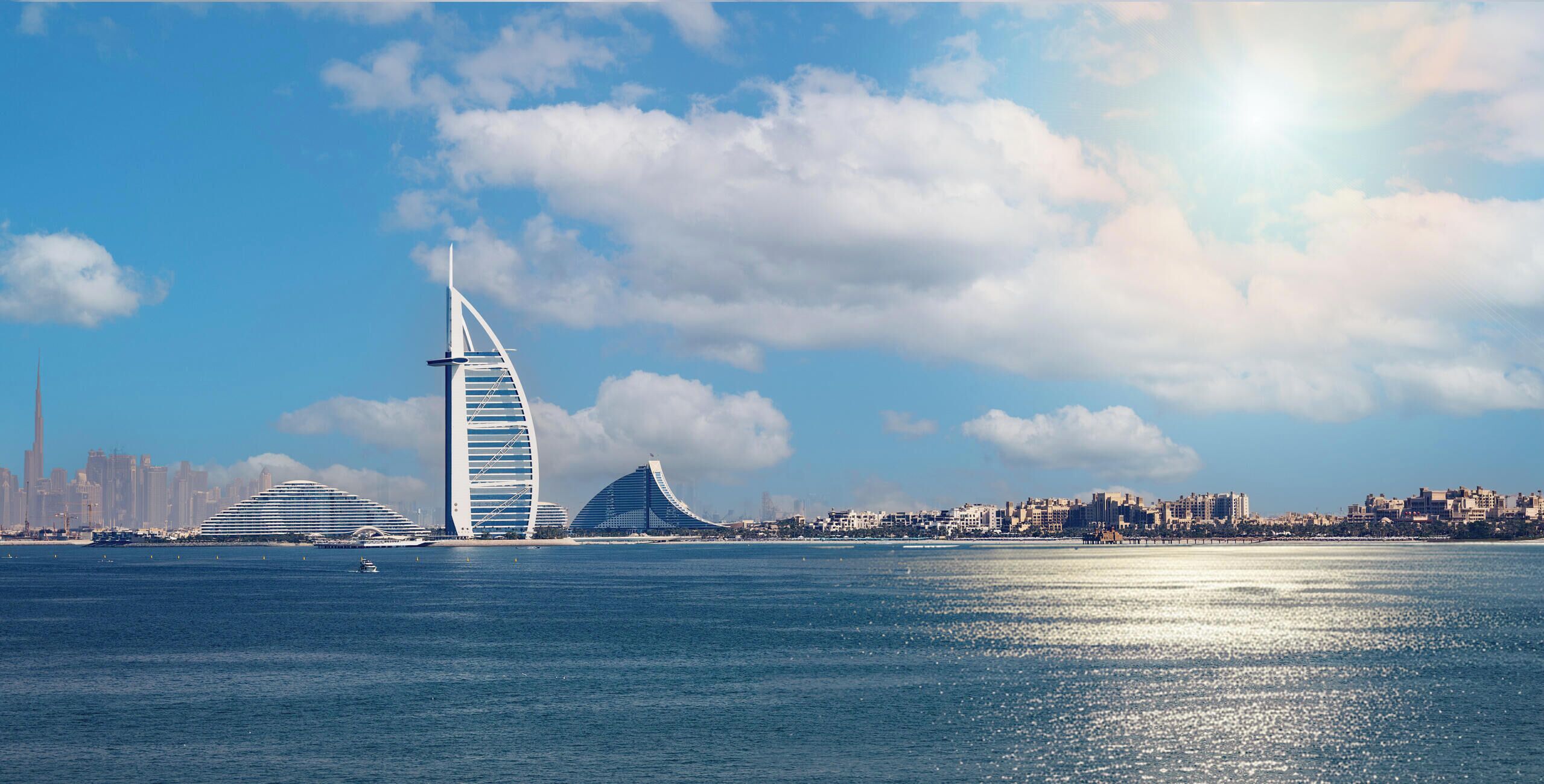 A coastal cityscape with prominent modern architecture, including a distinctive sail-shaped building and a large circular structure.