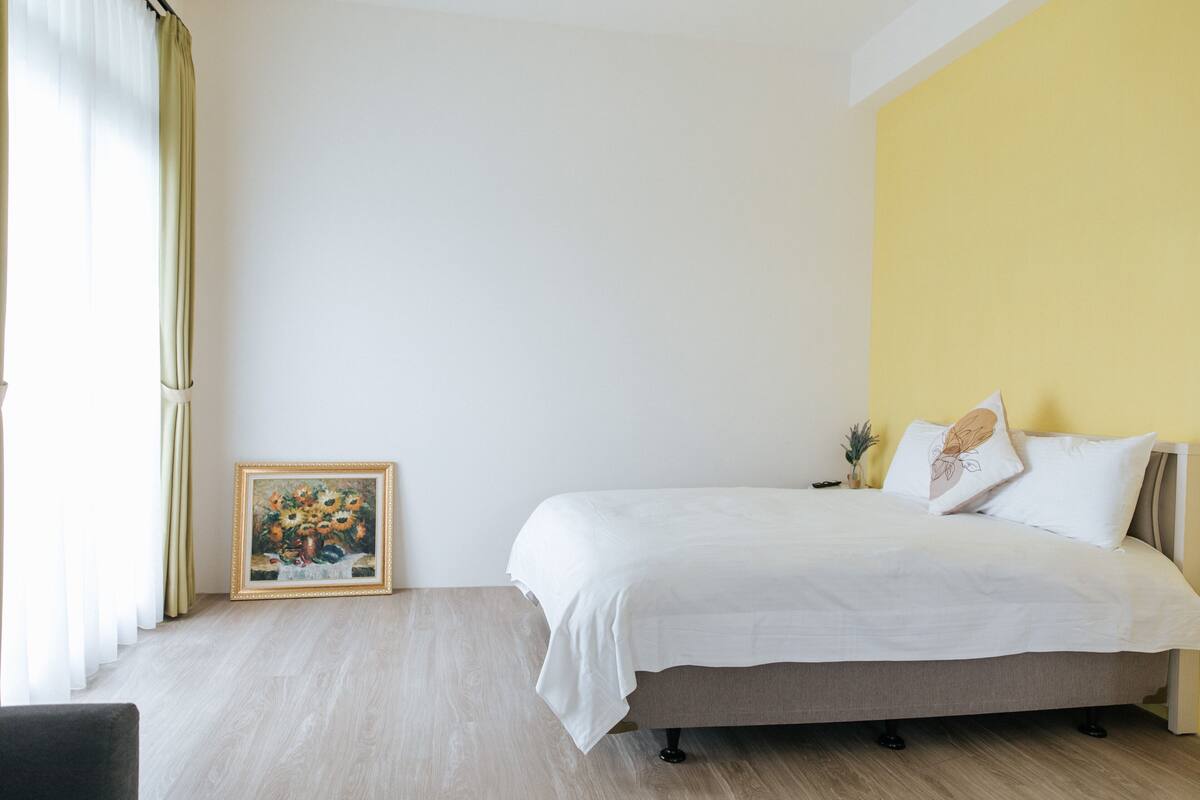 Quarto com cama, quadro emoldurado e parede amarela.