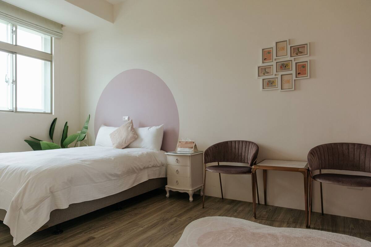 Quarto com cama, mesa de cabeceira, cadeiras e uma parede decorada com quadros.