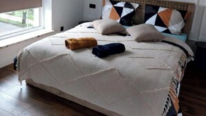 A bedroom with a large bed, a window with blinds, a wooden floor, and a plain white wall. - Inviting 1-bed Apartment in Lebork (Lebork)