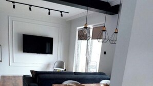 A modern living room with a dark blue sofa, a wooden dining table with placemats, and a flat-screen TV mounted on the wall. - Inviting 1-bed Apartment in Lebork (Lebork)