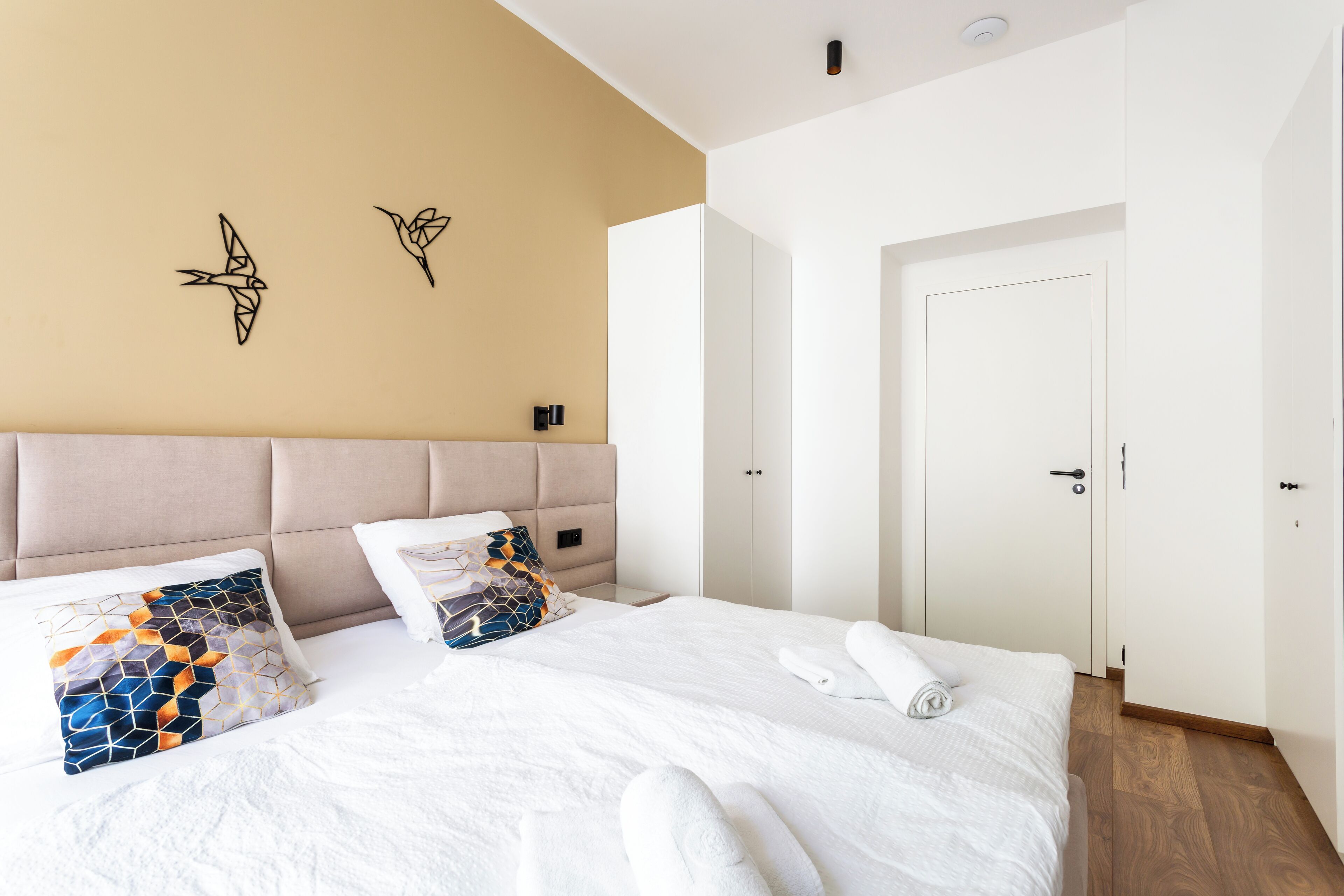 Hotelkamer met een groot bed, twee kussens, een hoofdeinde, een deur en een muur met twee decoratieve elementen.