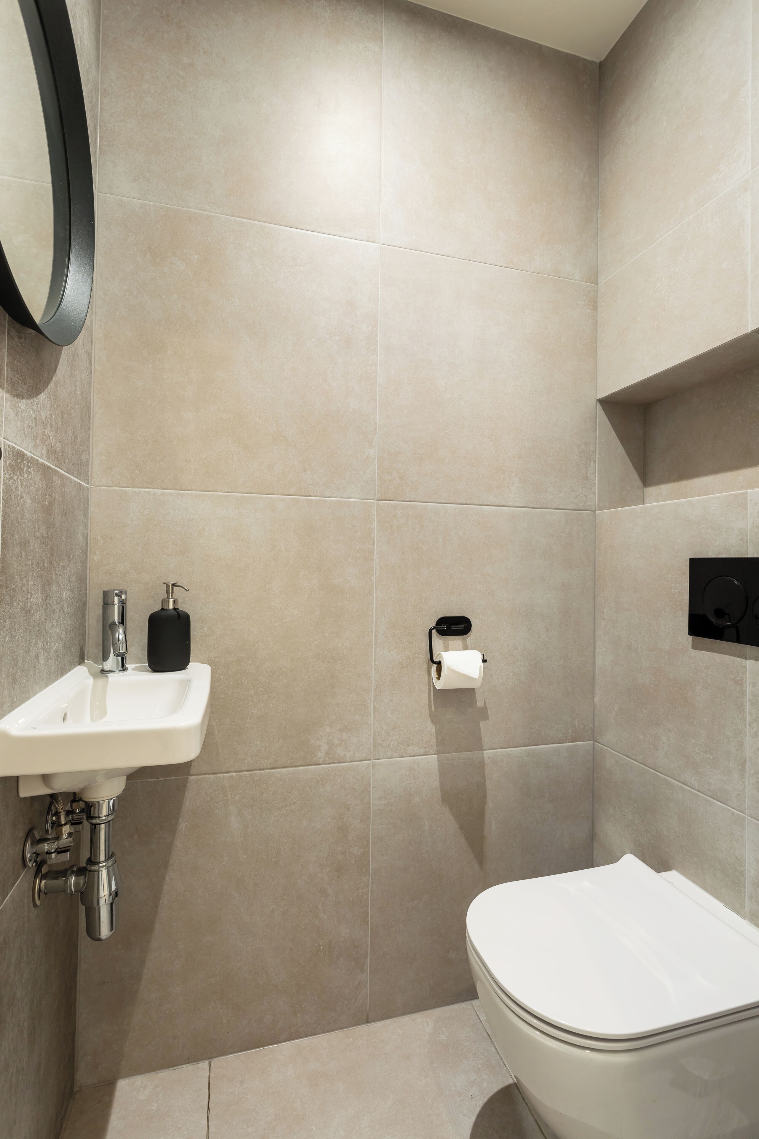 A modern bathroom with a toilet, sink, and a soap dispenser.