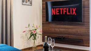 A modern living room with a large flat-screen TV displaying "NETFLIX," a blue sofa, a round coffee table with a bottle and glasses, and a decorative plant. - Luxury Residence Kmochova (Prague)