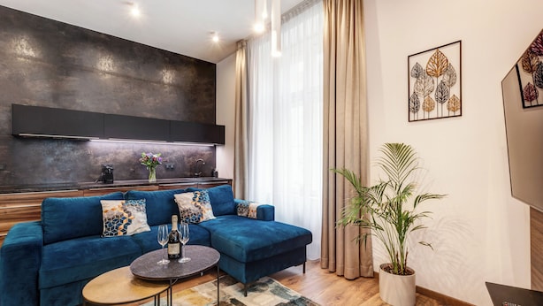 A modern living room with a blue sectional sofa, a round coffee table, and a potted plant. - Luxury Residence Kmochova (Prague)