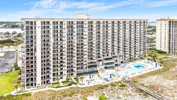 A high-rise hotel with multiple balconies, a swimming pool, and a landscaped area. - Beautiful Gulffront, Beachfront Phoenix VI Condo!! (Orange Beach)