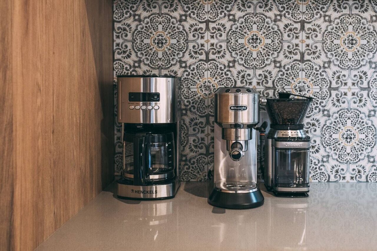 A coffee maker and a drip coffee maker on a countertop with a patterned backsplash.