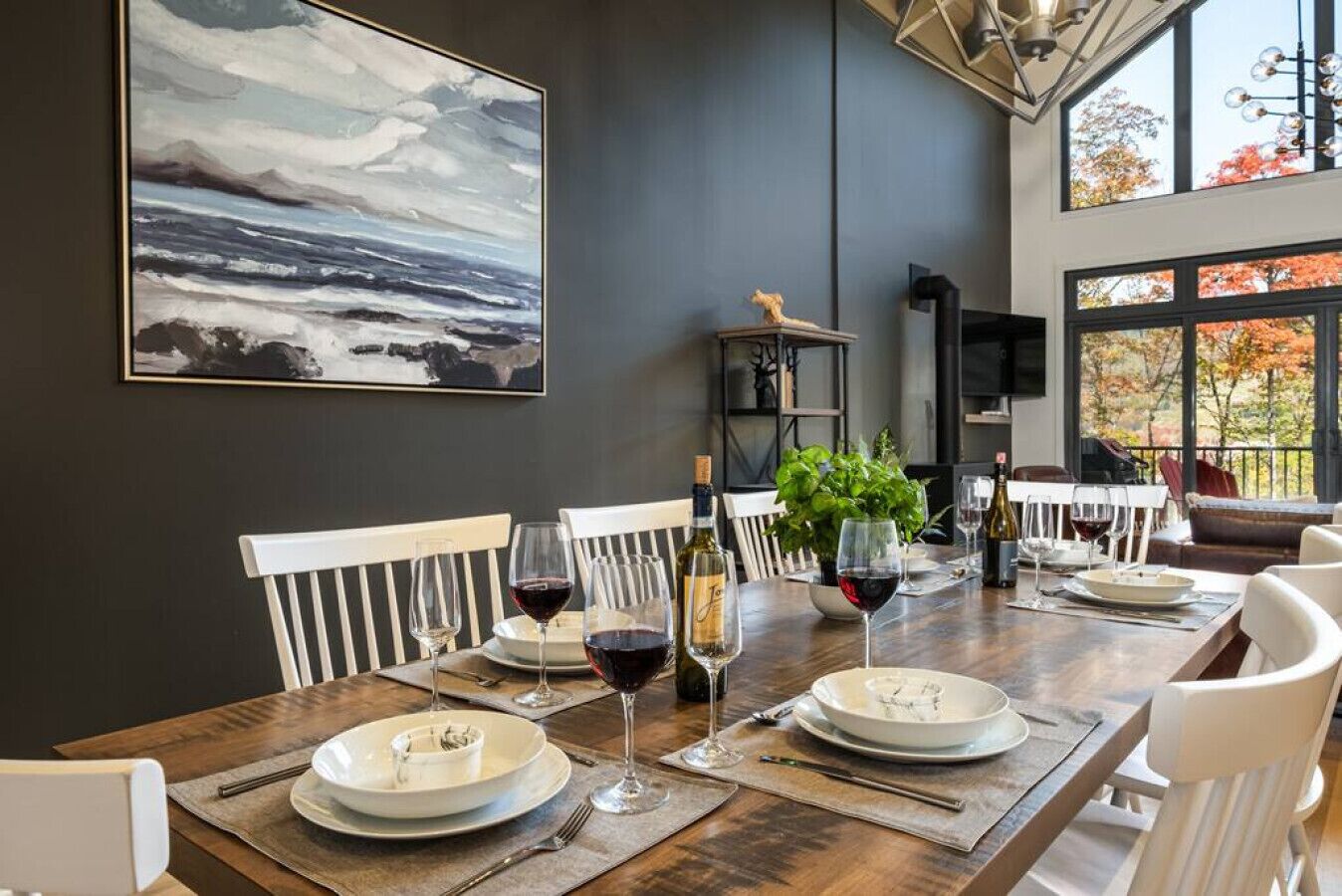 Comedor con una mesa de madera dispuesta para cuatro personas, sillas blancas y un cuadro abstracto grande en la pared.