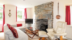 Un salón con chimenea de piedra, televisor, sofá y sillón de cuero.