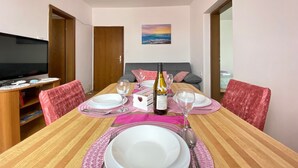 Un comedor con una mesa de madera dispuesta para cuatro personas, un televisor y un cuadro en la pared.