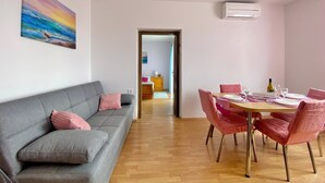 Una sala de estar moderna con un sofá gris, una mesa de comedor con sillas rosas y un cuadro de un atardecer en la pared.