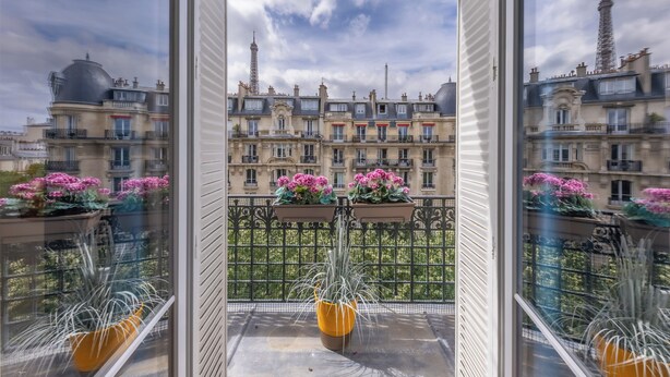 Varanda com vasos de plantas e vista para edifícios parisienses.