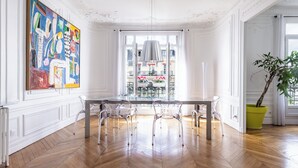Uma área de jantar com mesa e cadeiras, um quadro grande na parede e vista pela janela.
