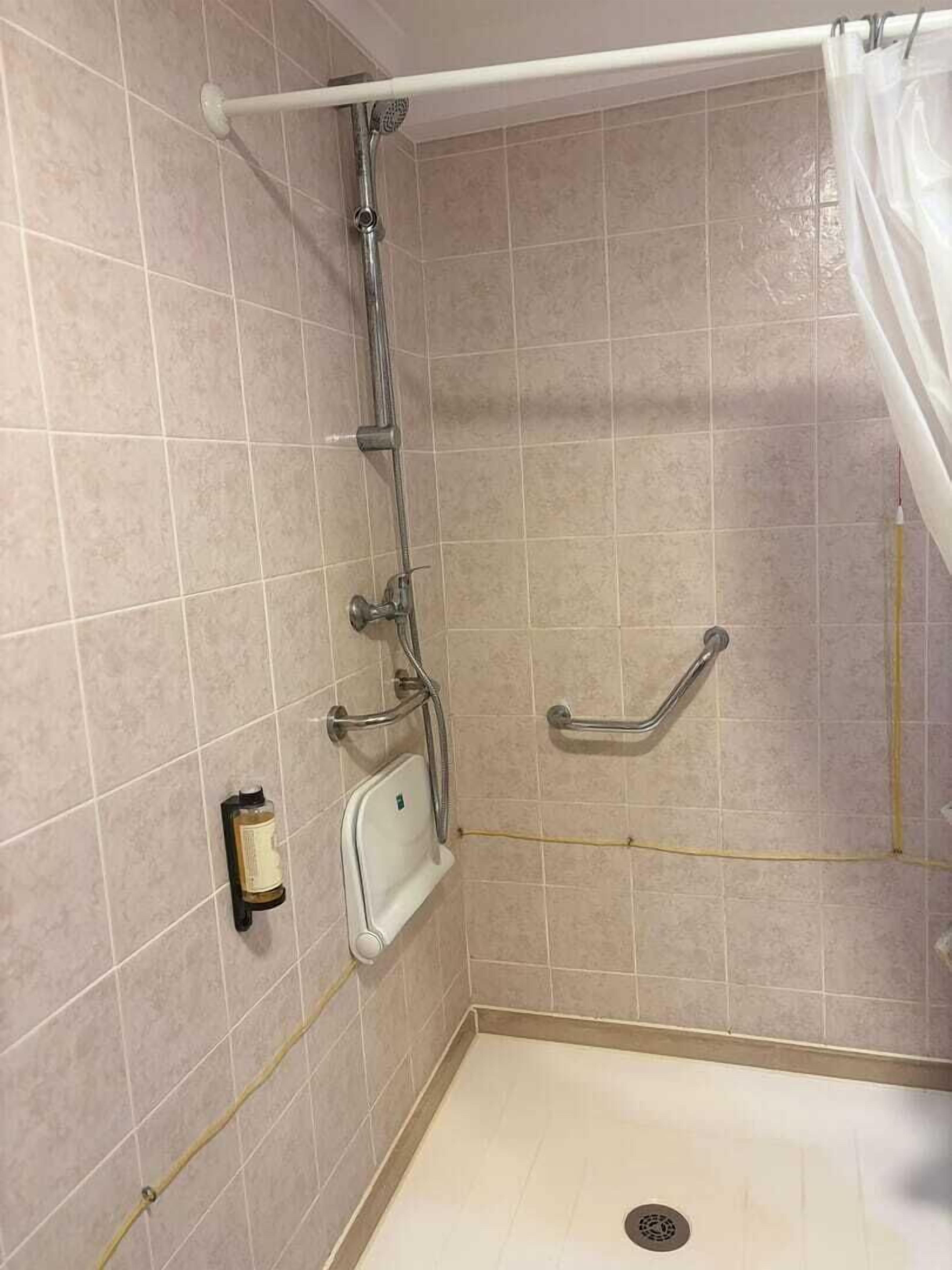 A small, enclosed shower area with a grab bar, a handheld showerhead, and a handheld soap dispenser.