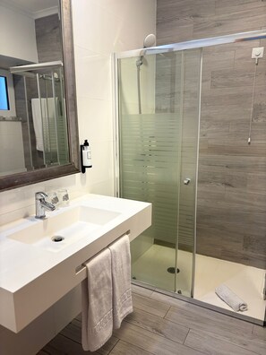 A modern bathroom with a glass-enclosed shower, a white sink with a mirror, and a towel on the floor. - BE ONE HOTEL Caldas da Rainha by MHMB Hospitality (Caldas da Rainha)