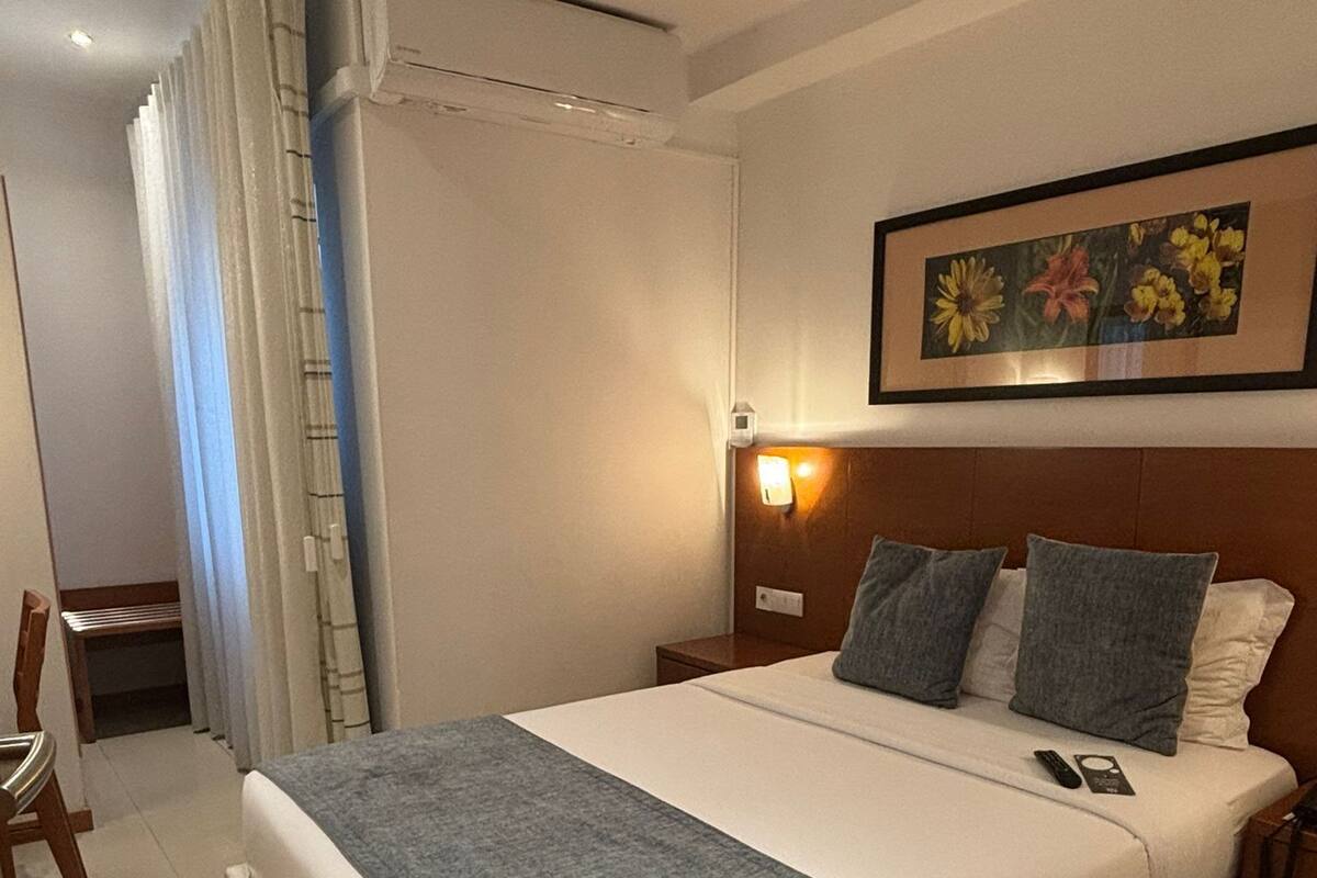 A hotel room with a large bed, a bedside table, a nightstand, a chair, a curtain, and a framed picture on the wall.