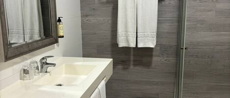 Un baño moderno con un espejo grande, un lavamanos, una ducha y suelo de madera.