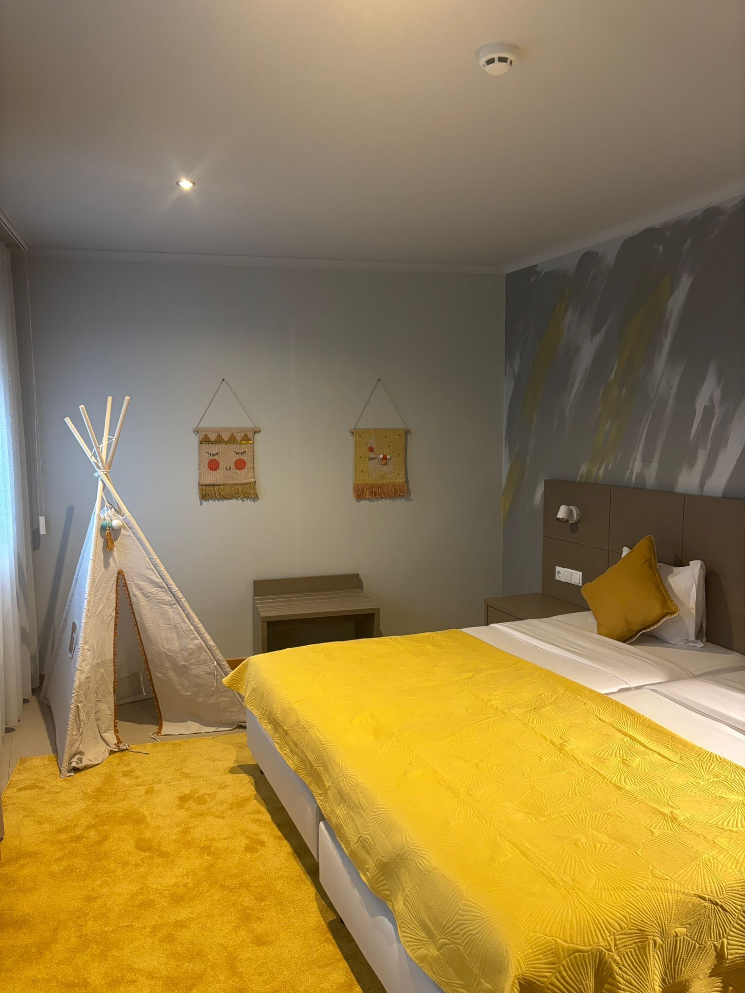 A bedroom with a bed, a nightstand, a bedside table, a wall-mounted lamp, and a painting.