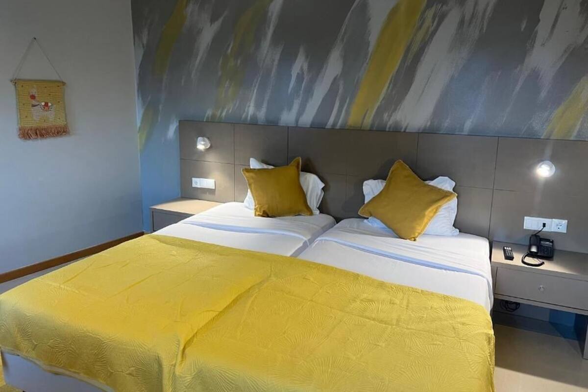 A double bed with a yellow bedspread, two bedside tables with lamps, and a modern abstract wall painting.