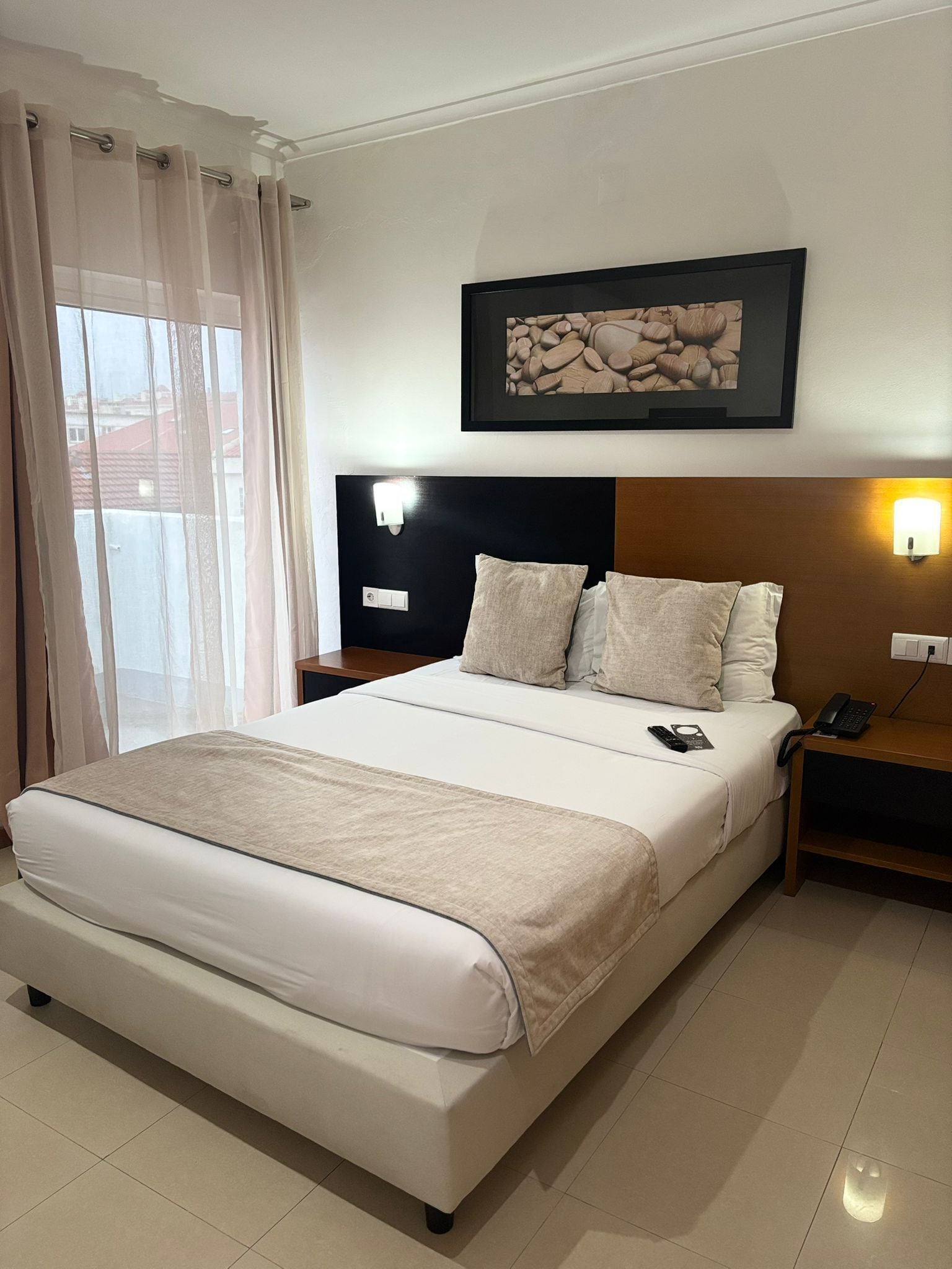 Habitación de hotel con una cama grande, cabecera con lámpara y mesita de noche con teléfono, además de un cuadro en la pared.