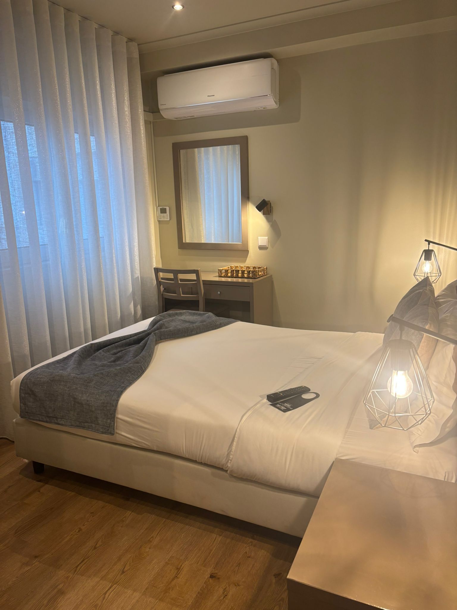 Une chambre d’hôtel moderne avec un grand lit, un bureau et une fenêtre équipée de stores.