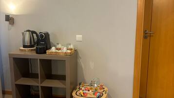 Sala de estar com televisão de tela plana na parede, cafeteira, chaleira e uma pequena mesa com brinquedos.