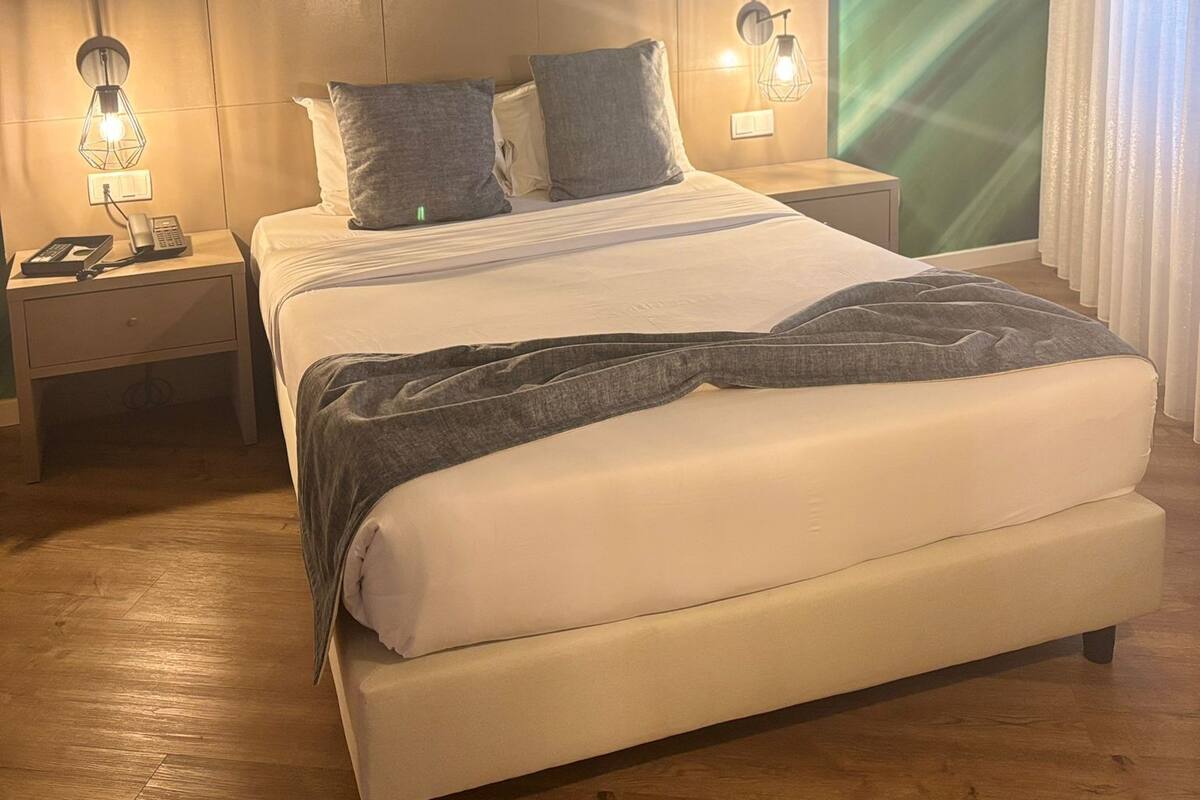 A modern hotel room with a large bed, two bedside tables, and a green abstract wall design.
