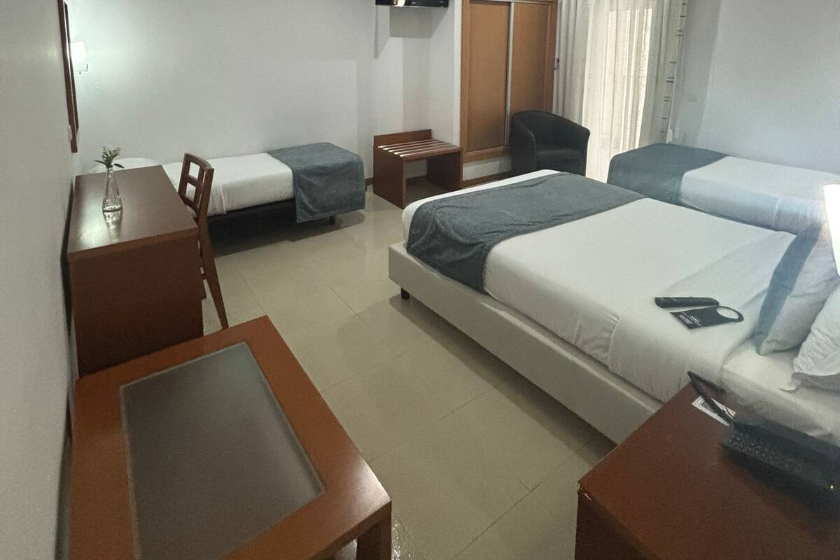 A hotel room with a bed, a desk, a chair, a TV, and a wardrobe.