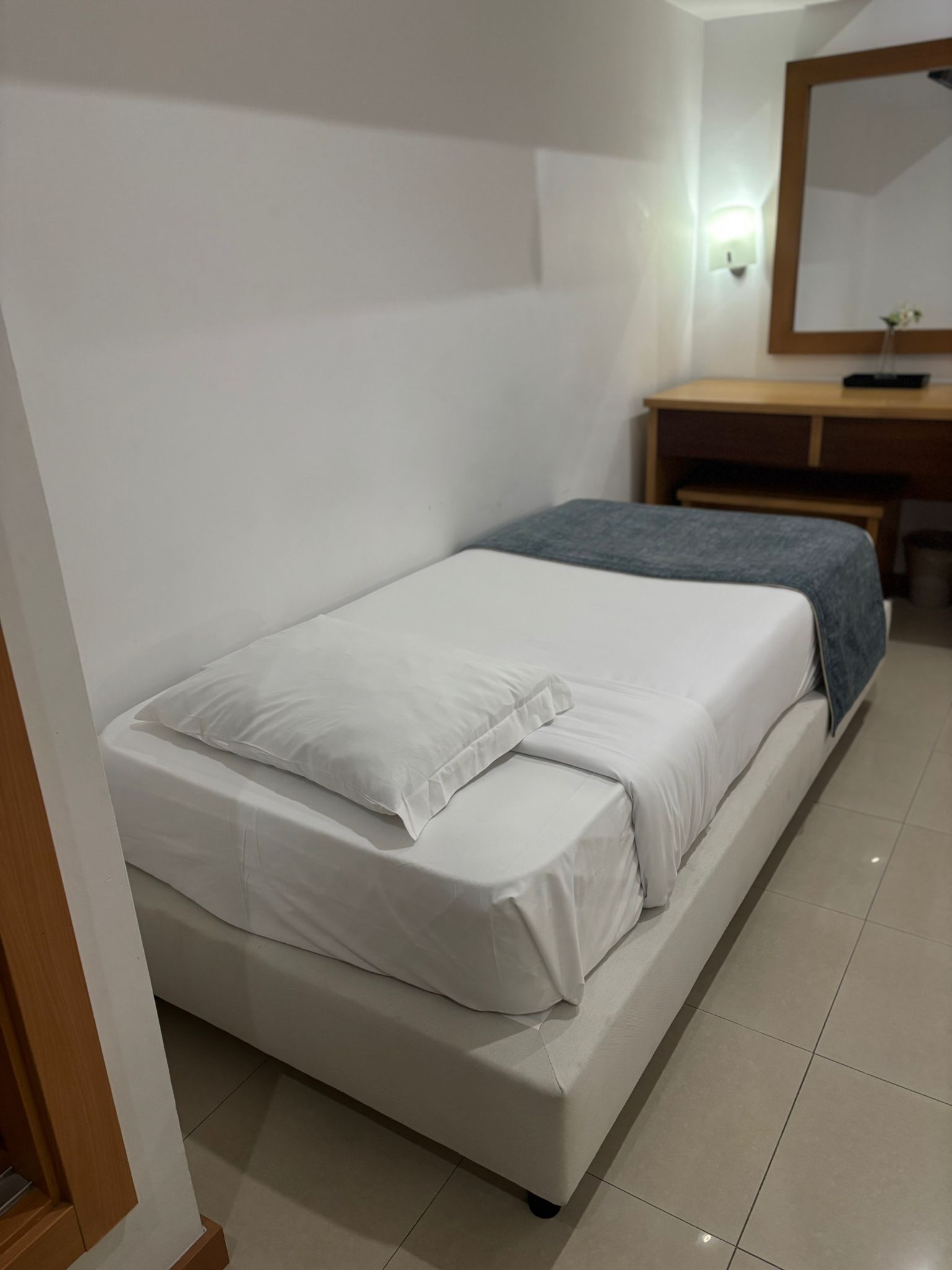 Une chambre avec un lit simple, un bureau en bois et un miroir.