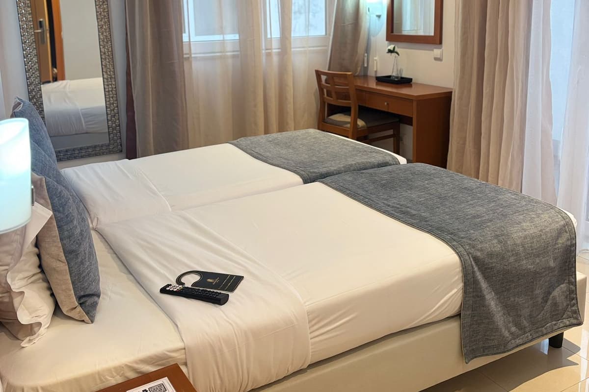 A hotel room with a large bed, a desk, a chair, a TV, and a mirror.