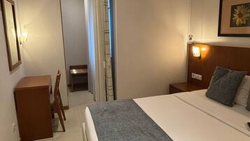 Habitació d'hotel amb un llit gran, una taula de treball, una cadira, una nitòria i un aire condicionat fixat a la paret.