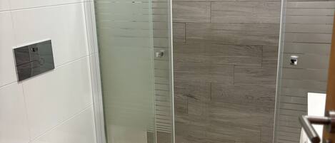 A modern bathroom with a glass-enclosed shower, a toilet, and a trash bin.