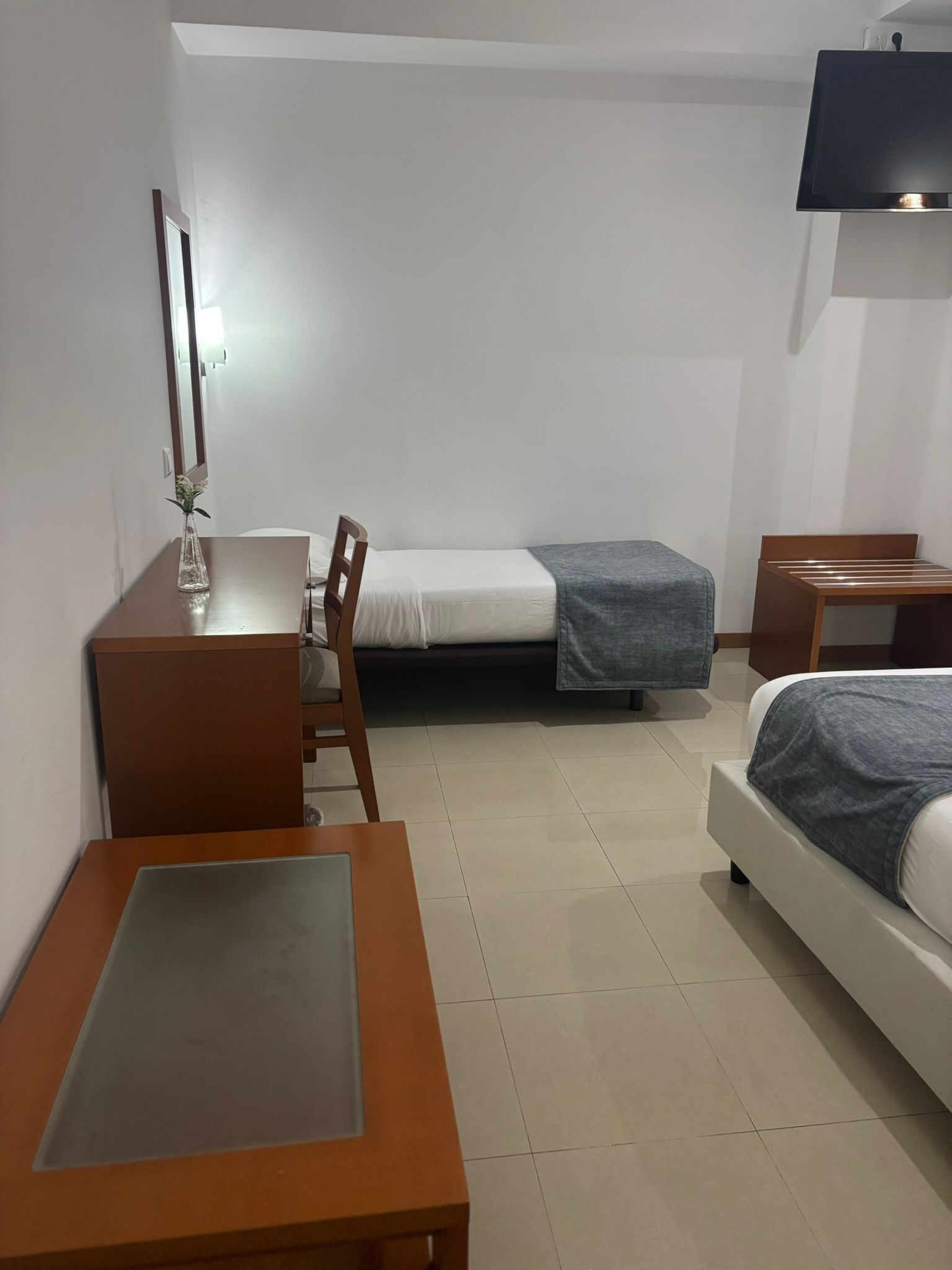 Habitación de hotel pequeña con una cama individual, un escritorio, una silla y un televisor montado en la pared.