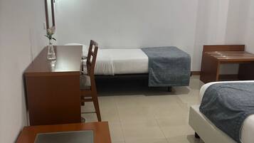 Habitación de hotel pequeña con una cama individual, un escritorio, una silla y un televisor montado en la pared.