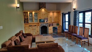 A living room with a fireplace, wooden cabinets, and a seating area with a sofa and chairs. - Nature Roar Forest Resort (Nainital)