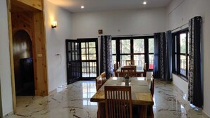 A spacious dining area with a marble floor, wooden furniture, and large windows with curtains. - Nature Roar Forest Resort (Nainital)