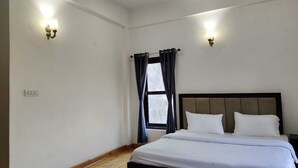 A bedroom with a bed, two wall sconces, a window with curtains, and a wooden floor. - Nature Roar Forest Resort (Nainital)