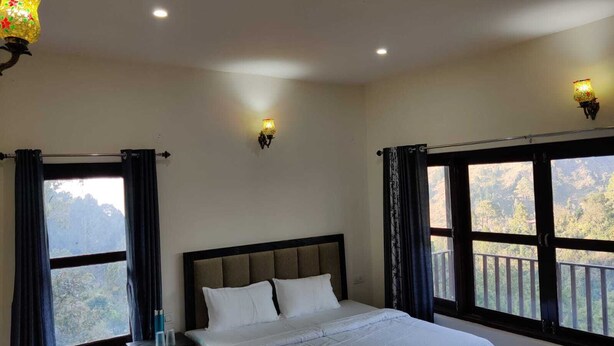 A bedroom with a bed, two wall sconces, a window with curtains, and a decorative lamp. - Nature Roar Forest Resort (Nainital)