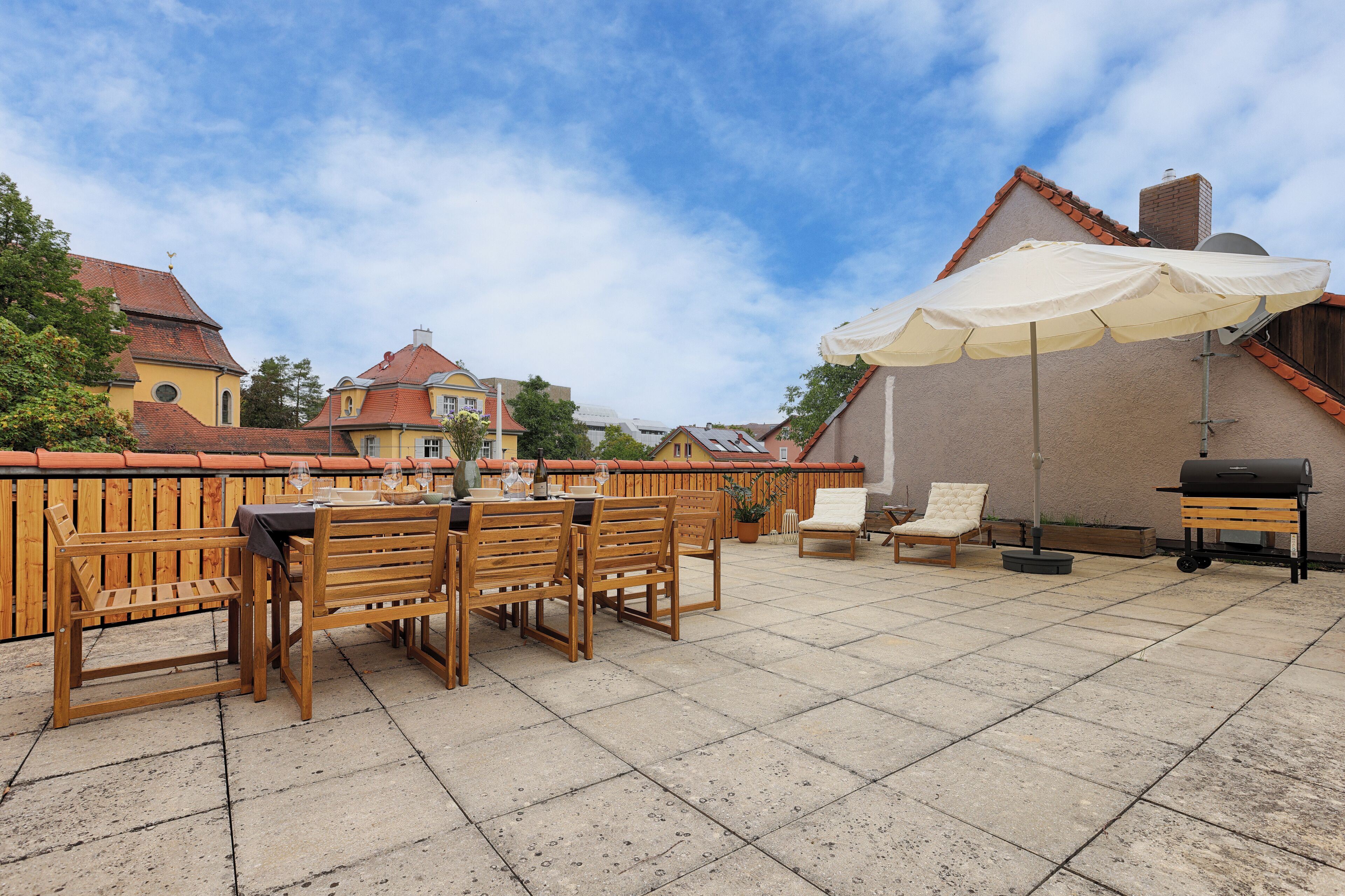 Une terrasse avec une table et des chaises, un barbecue et un grand parasol.