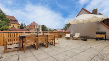 Une terrasse avec une table et des chaises, un barbecue et un grand parasol.