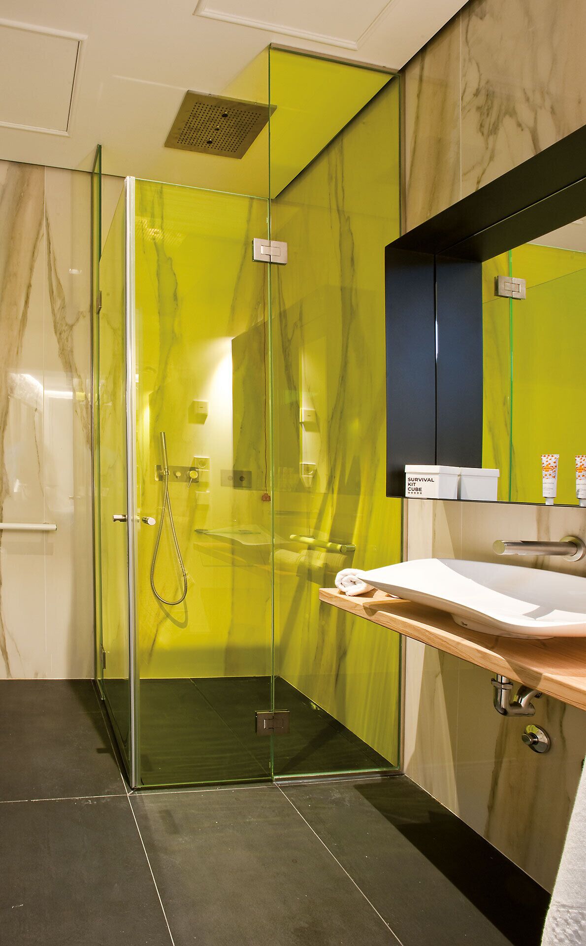 A modern bathroom with a glass-enclosed shower, a marble-tiled wall, a wooden vanity, and a black cabinet.