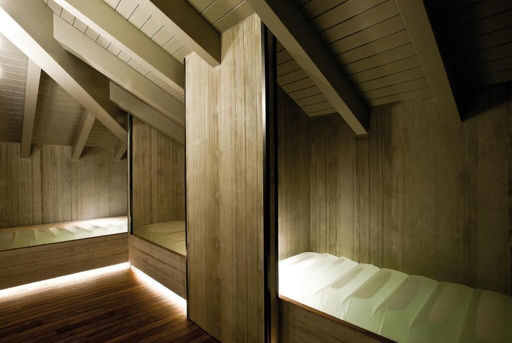 Una habitación con paredes y techo de madera, una cama con ropa de cama blanca y un tragaluz.