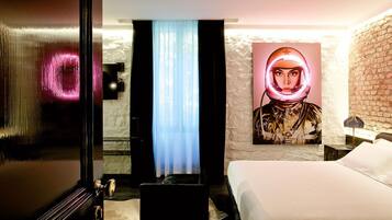 Ein Hotelzimmer mit einem Bett, einem großen Bild eines Raumanzugs, einer Backsteinwand und einer Tür mit spiegelnder Oberfläche.