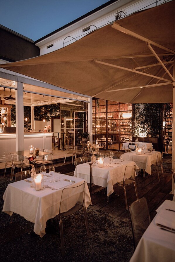 An outdoor dining area with tables set for a meal, covered by a large canopy, and surrounded by a rustic wooden deck. - Areadocks Boutique Hotel (Brescia)