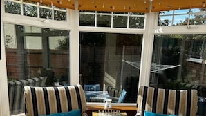 A conservatory with two striped armchairs and a small table, large windows, and a view of the outside. - 4 Hilbre - Seaside Retreat Sheringham  (Sheringham,)