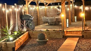 A wooden pergola with string lights, a barbecue grill, and outdoor seating. - 4 Hilbre - Seaside Retreat Sheringham  (Sheringham,)