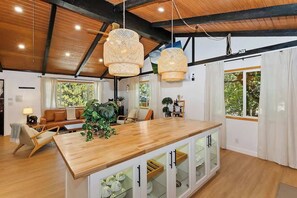 A spacious living area with a wooden island, white cabinets, and a large window with curtains. - Eagle Peak Walk to Village & Lake Fire Pit (Big Bear Lake)