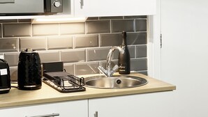 A modern kitchen with a stainless steel sink, a kettle, and a wine bottle on the counter. - Erin Court Mansion -Suite 11 (South Croydon)