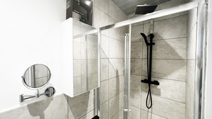 A modern bathroom with a glass-enclosed shower, a round mirror, and a hair dryer on a shelf. - Erin Court Mansion -Suite 11 (South Croydon)